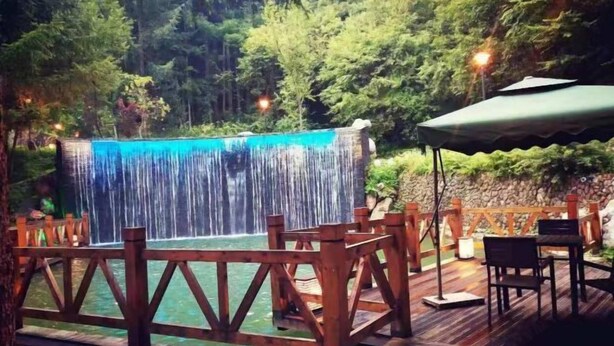 A wooden deck with a waterfall feature, surrounded by a wooden fence and an umbrella.