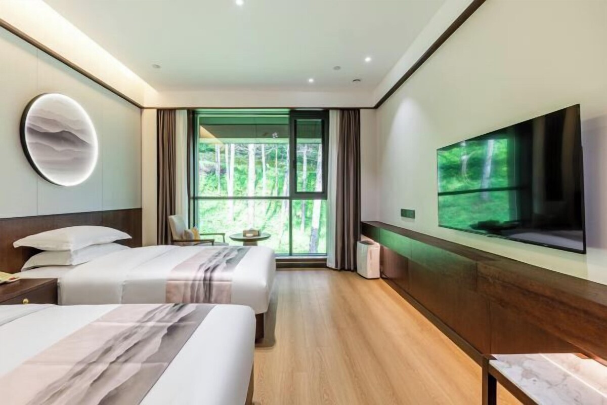 Habitación de hotel moderna con dos camas, un televisor grande y un balcón con vistas a zonas verdes.