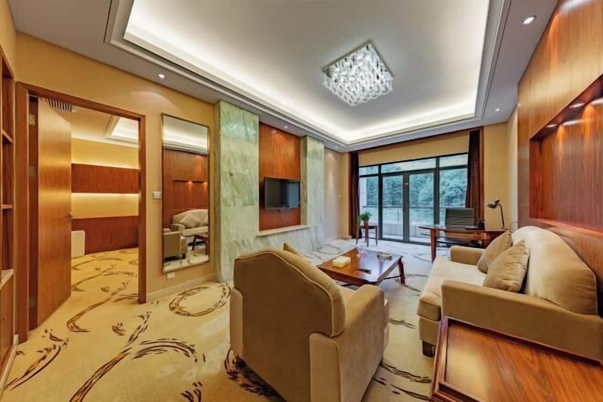 Una habitación de hotel moderna con sofá, una mesa de centro, televisor y un ventanal grande.