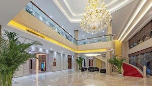 A spacious lobby with a high ceiling, a grand chandelier, and a red staircase.