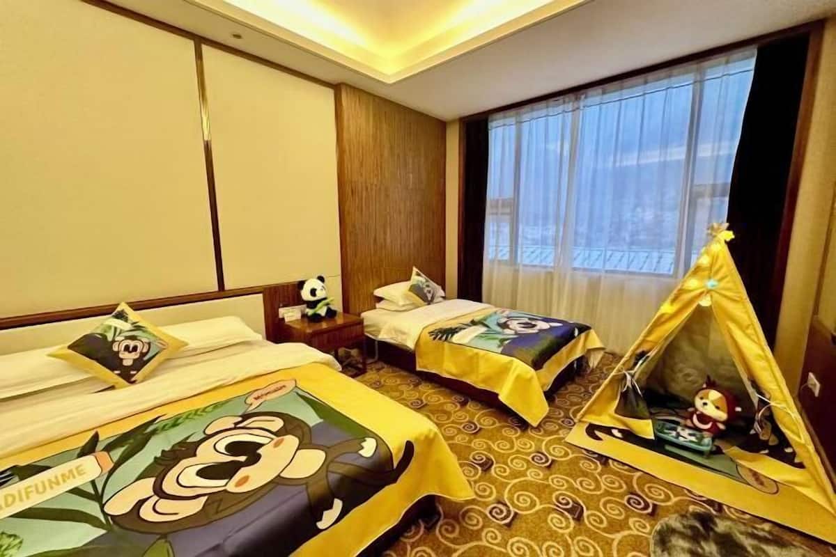 Habitación de hotel con dos camas, una ventana con cortinas, una mesita con lámpara y una estructura parecida a una tienda de campaña con juguetes.