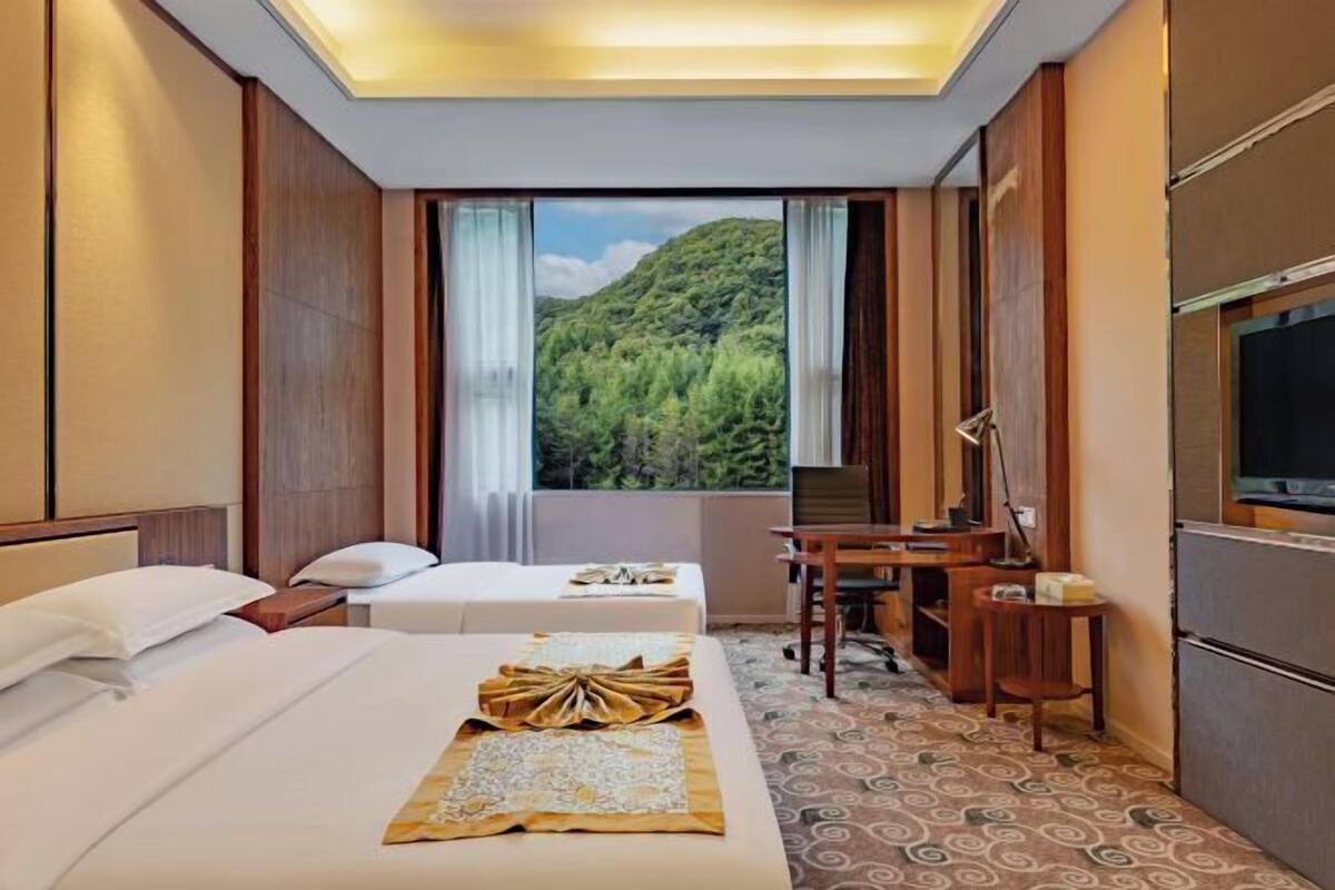 Habitación de hotel con dos camas, un escritorio, una silla, un televisor y una ventana con vista al bosque.