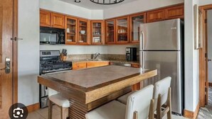 Una cucina con mobili in legno, un frigorifero in acciaio inox, un'isola integrata con sgabelli da bar e un forno a microonde.