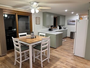 A modern kitchen with a dining table, white chairs, a ceiling fan, and light-colored cabinets. - Gary's Game-Day Getaway only 1.4 miles from Lambeau! (Green Bay)