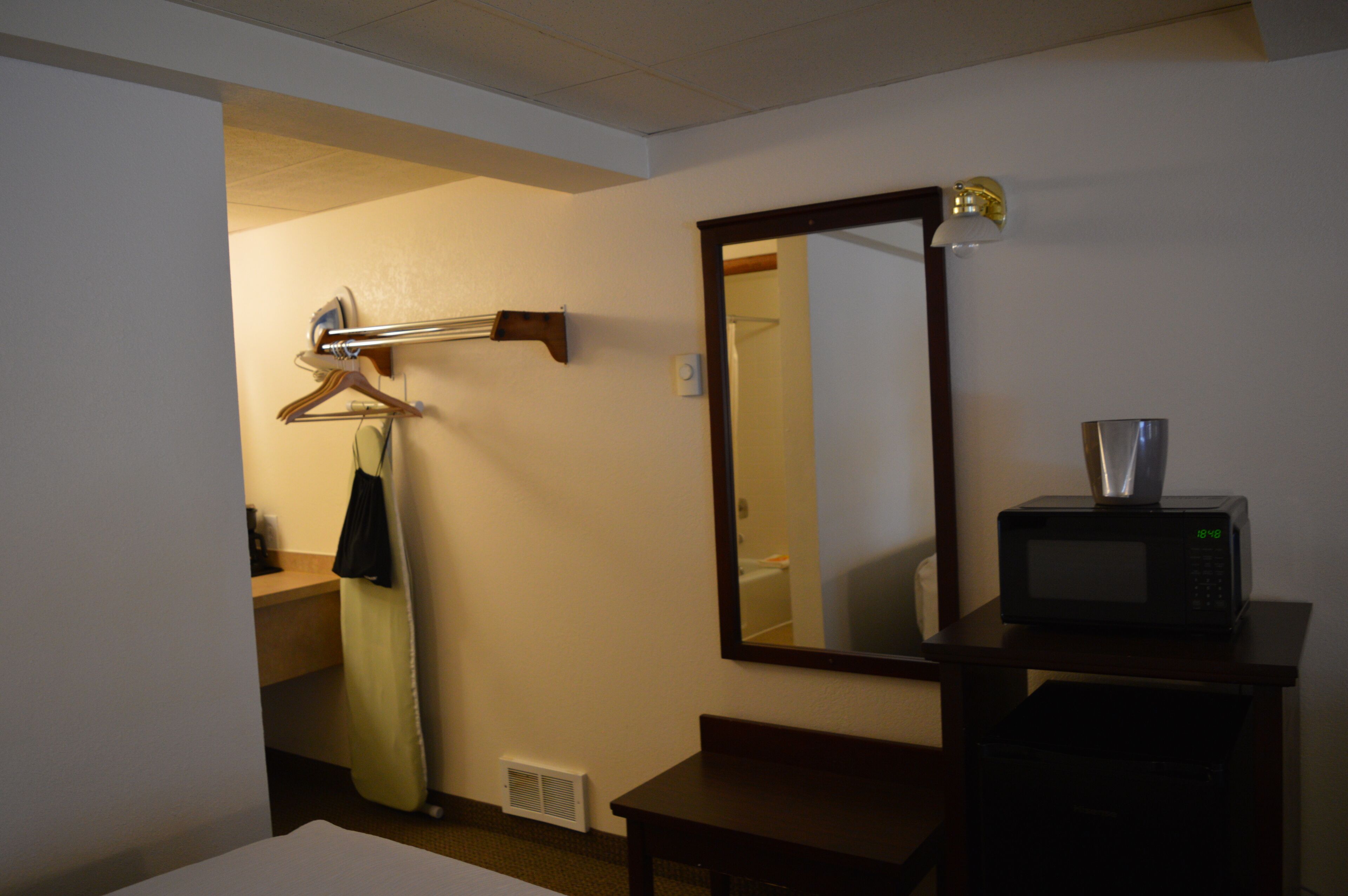 Hotelkamer met een bed, nachtkastje met een magnetron, spiegel en kledingrek.