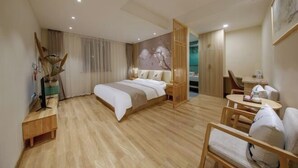 Een moderne hotelkamer met een houten vloer, een bed met witte lakens, een bureau met een lamp en een stoel.