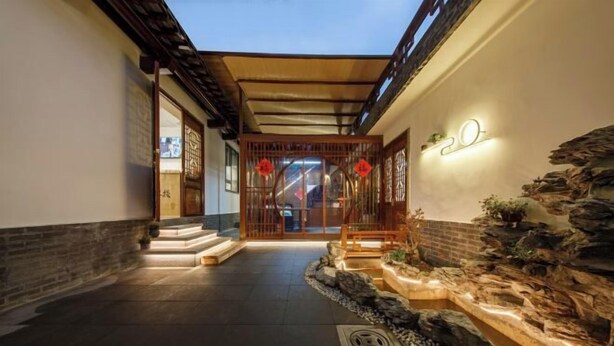 Een traditionele Japanse entree met een houten poort, een stenen muur met beplanting en een kleine rotstuin.