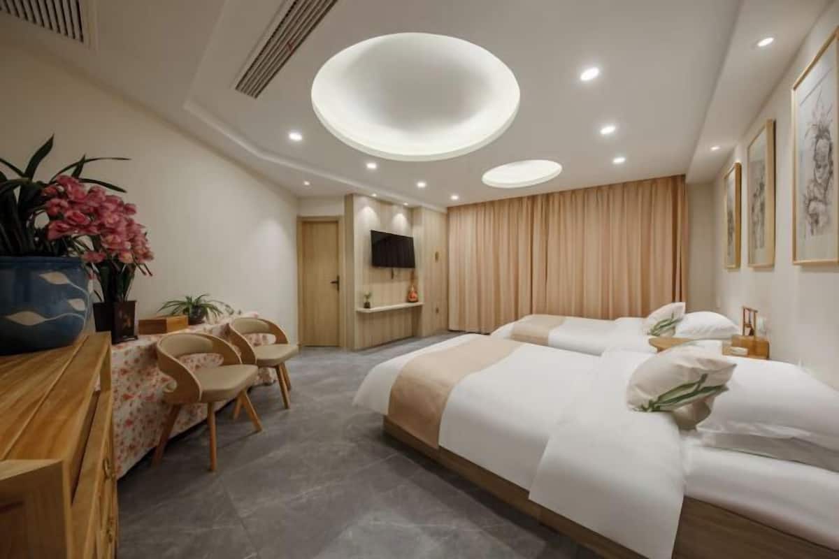 A modern hotel room with a large bed, a desk, chairs, a television, and a ceiling light fixture.