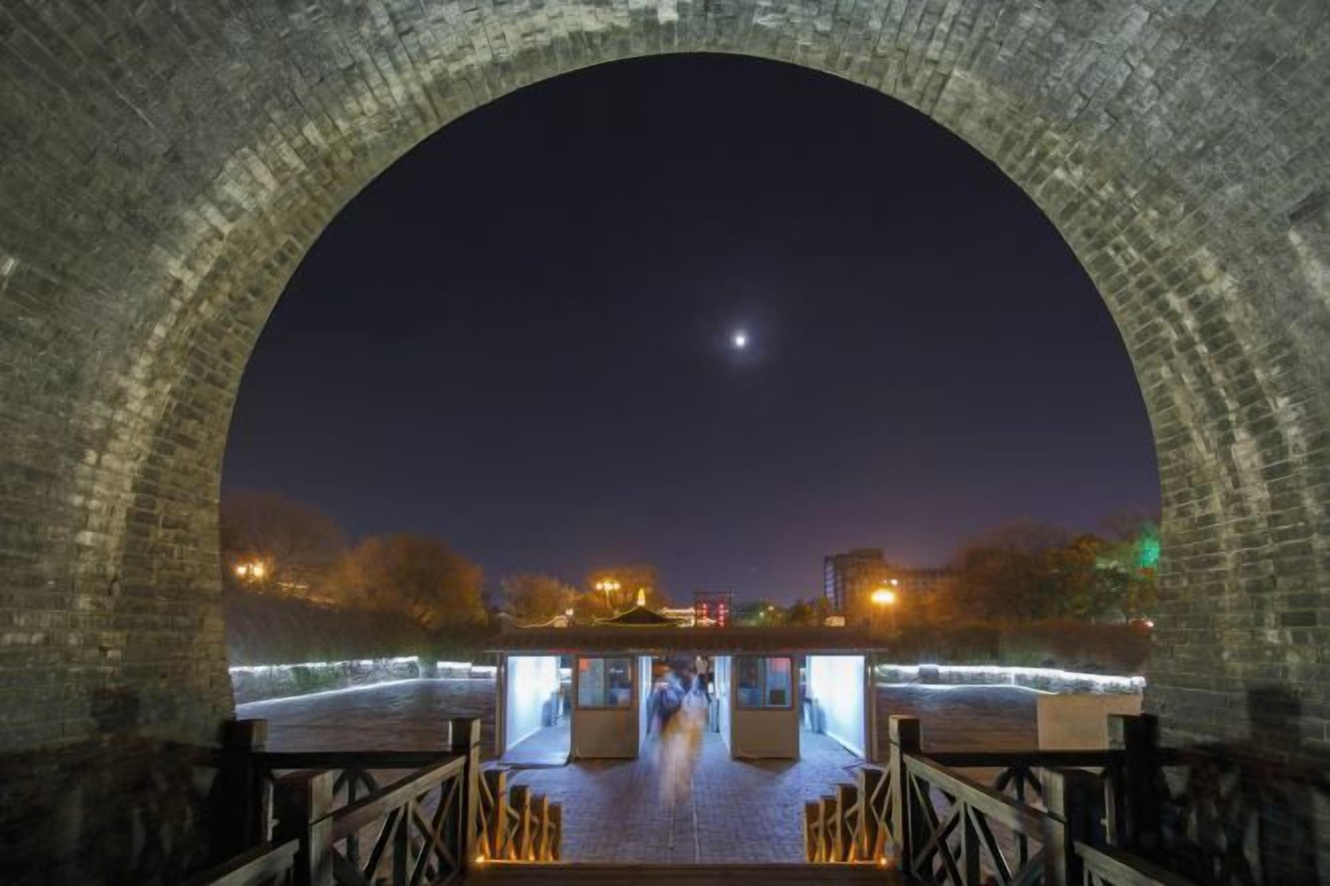 A brick archway with a view of a cityscape at night.