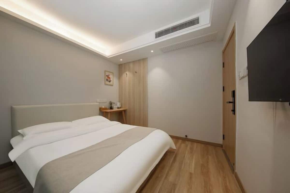 A modern hotel room with a large bed, a bedside table, a TV mounted on the wall, and a wardrobe.
