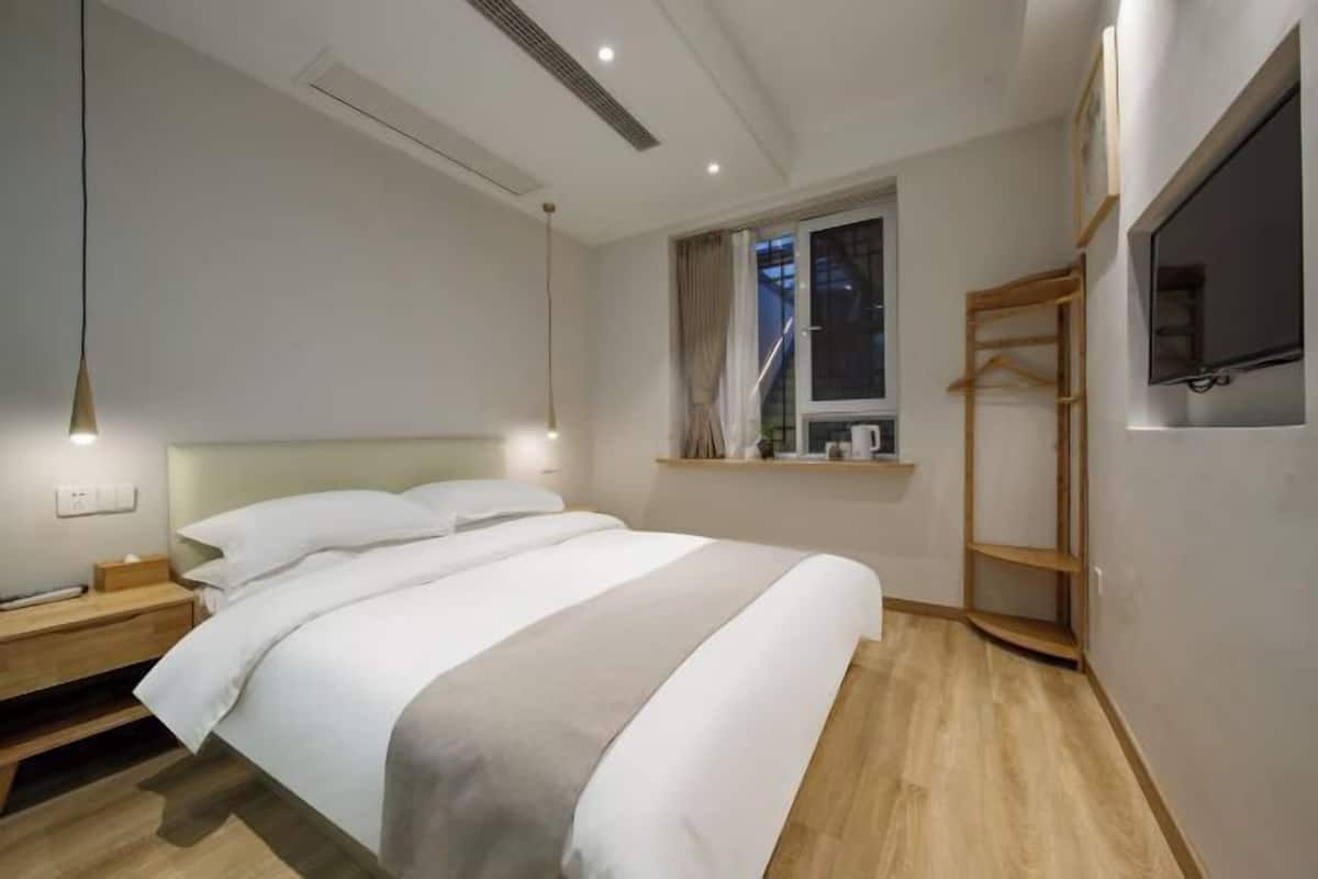 A modern hotel room with a large bed, bedside tables, a TV, and a window with curtains.