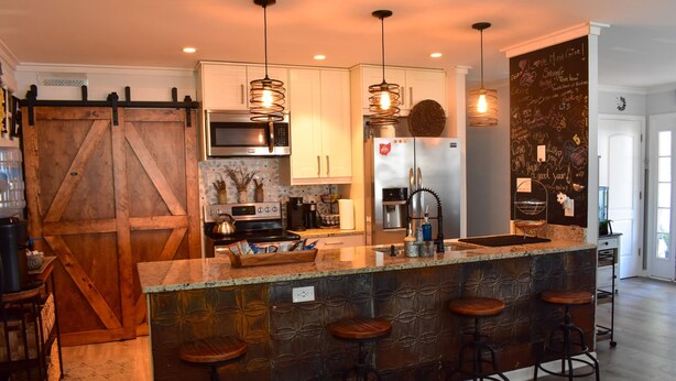 Una cocina con una isla grande, taburetes de bar, una puerta corredera estilo granero y una pared de pizarra.