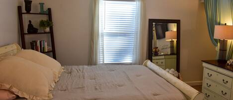 A bedroom with a bed, a dresser, a mirror, and a shelf with books and decorative items.