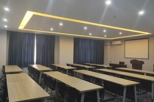 Un salón de conferencias con varias mesas y sillas, un atril y una pantalla de proyector.
