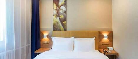 Habitación de hotel con una cama grande, dos mesitas de noche con lámparas, una obra de arte en la pared y una ventana con cortinas.