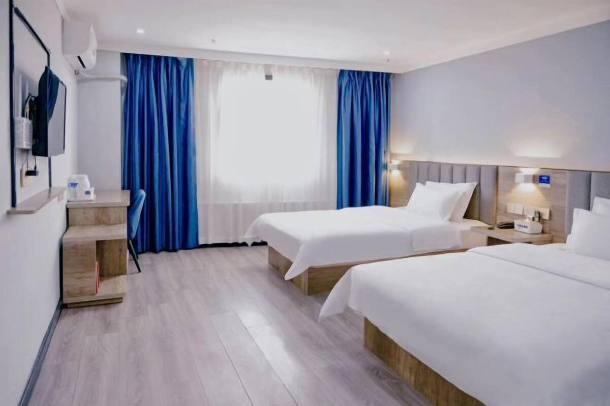 A hotel room with two beds, a desk, a chair, a TV, and a window with curtains.