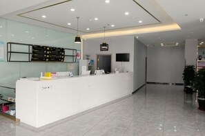 A reception area with a white reception desk, a flat-screen TV, and a glass wall. - 7 Days Premium (Zibo Zichuan Hongtai) (Zibo)