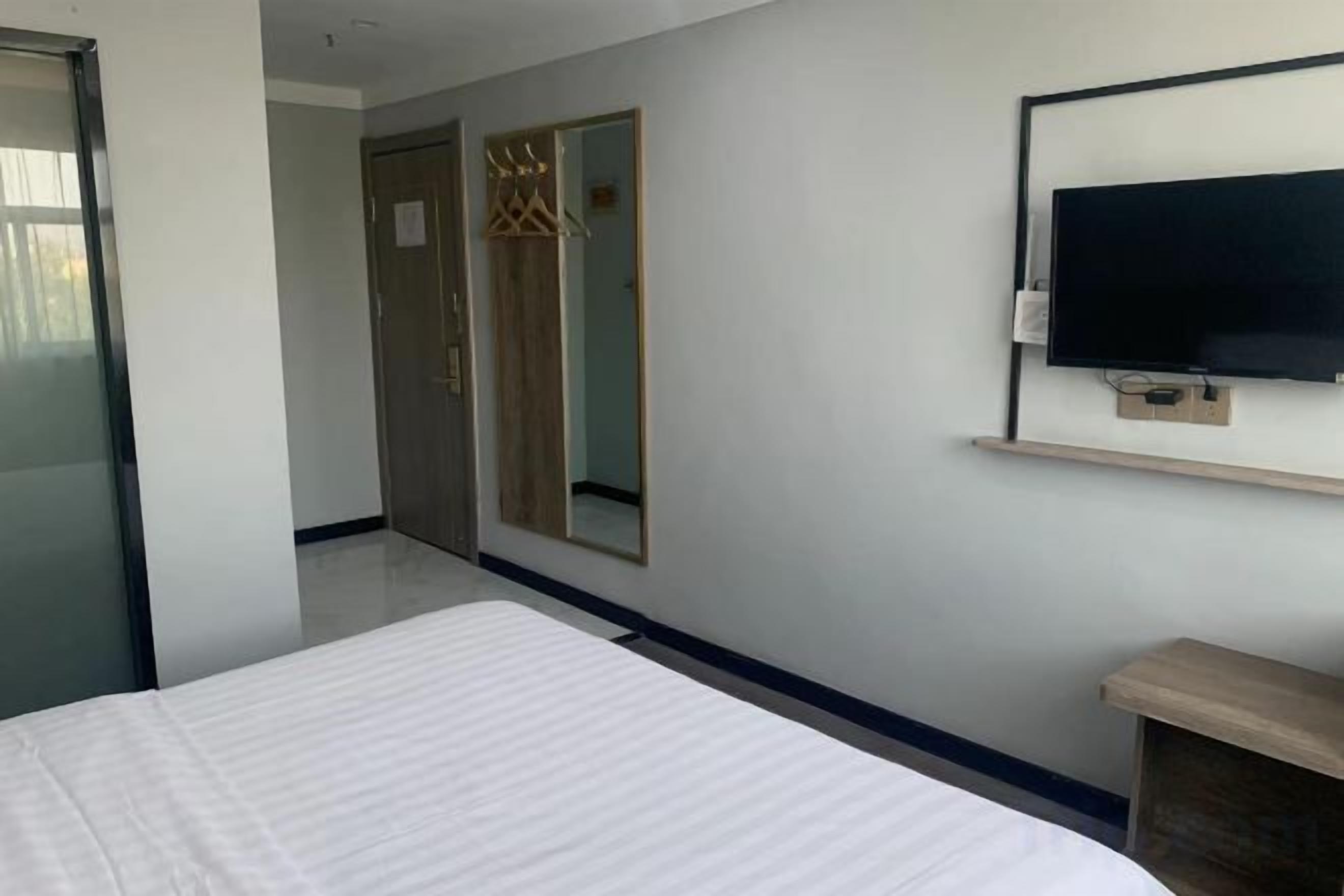 Ein Hotelzimmer mit einem Bett, einem an der Wand befestigten Fernseher, einem Spiegel und einem Kleiderschrank.