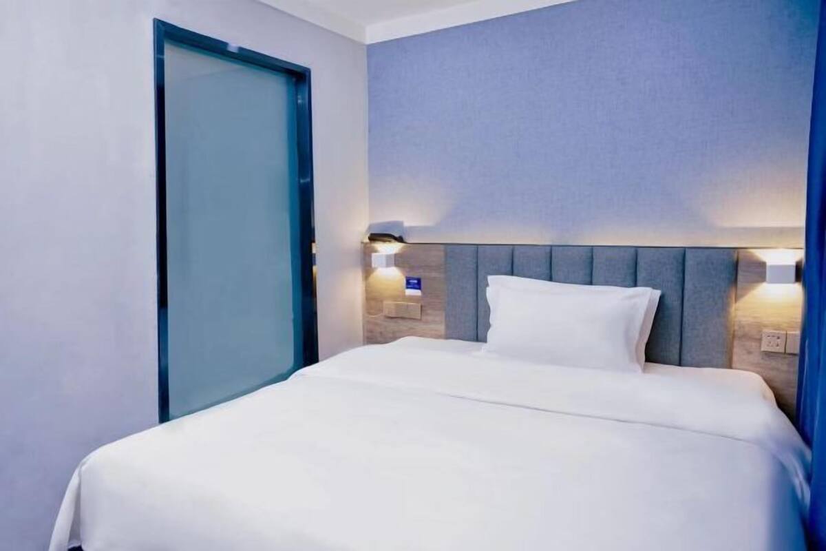 A hotel room with a bed, a door, and wall-mounted lights.