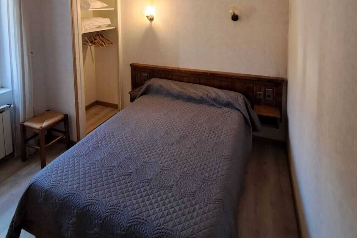 A small, single-bed room with a wooden headboard, a bedside table, and a closet with a hanging rack.
