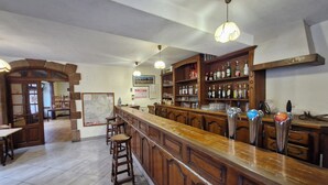 A bar area with a wooden counter, stools, and a variety of bottles on shelves. - le relais de lassouts (Lassouts)
