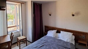 A hotel room with a bed, a desk, and a chair. There is a window with curtains, and a door is visible. - le relais de lassouts (Lassouts)