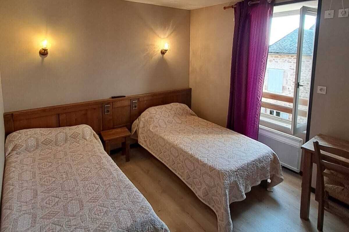 A room with two single beds, a wooden bench, a table, and a window with a view.