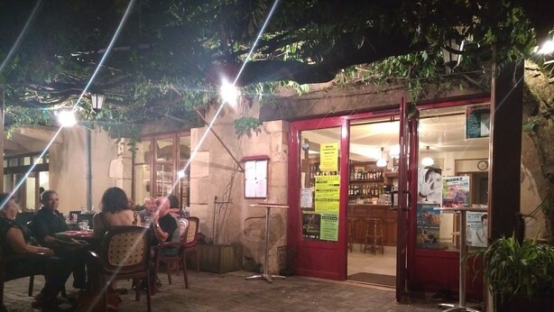 An outdoor café with tables and chairs, a red door, and a signboard with text. - le relais de lassouts (Lassouts)