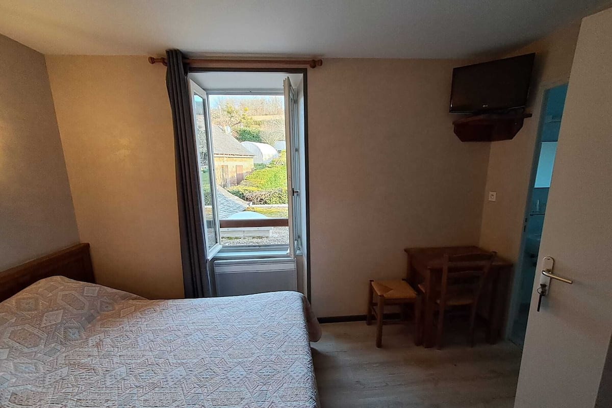 A hotel room with a bed, a small desk, a chair, and a television mounted on the wall.