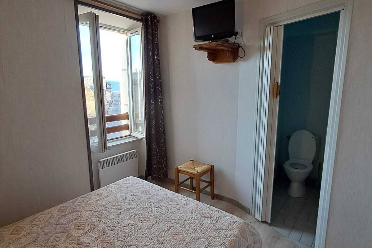 A bedroom with a bed, a television mounted on the wall, a small stool, and a bathroom door.