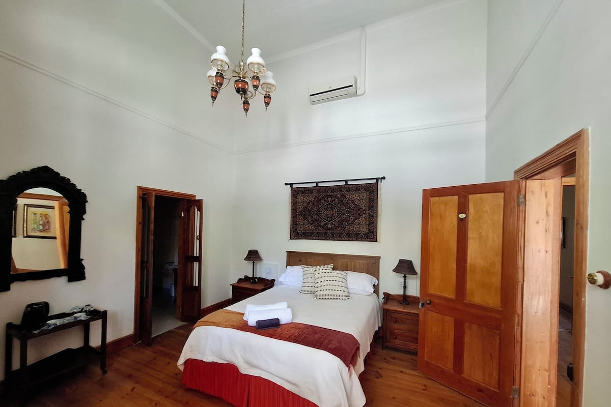 A bedroom with a wooden bed, a chandelier, a wall-mounted air conditioner, and a wooden door.