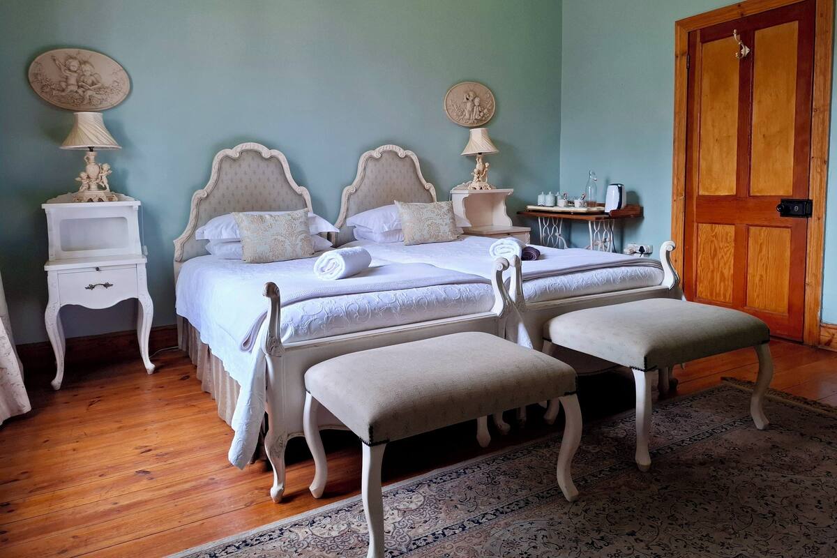 A bedroom with two beds, a wooden door, and a small table with a lamp.