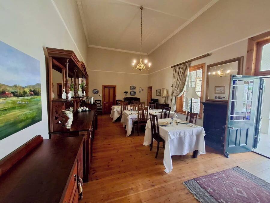Uma sala de jantar com mesas e cadeiras de madeira, um candelabro e um quadro na parede.