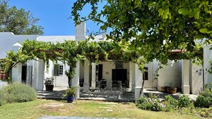 A white building with a covered patio area, potted plants, and a clear blue sky. - Sundays Karoo Guesthouse (Graaff-Reinet)