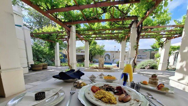 A breakfast table set outdoors with plates of food, utensils, and a beverage. - Sundays Karoo Guesthouse (Graaff-Reinet)