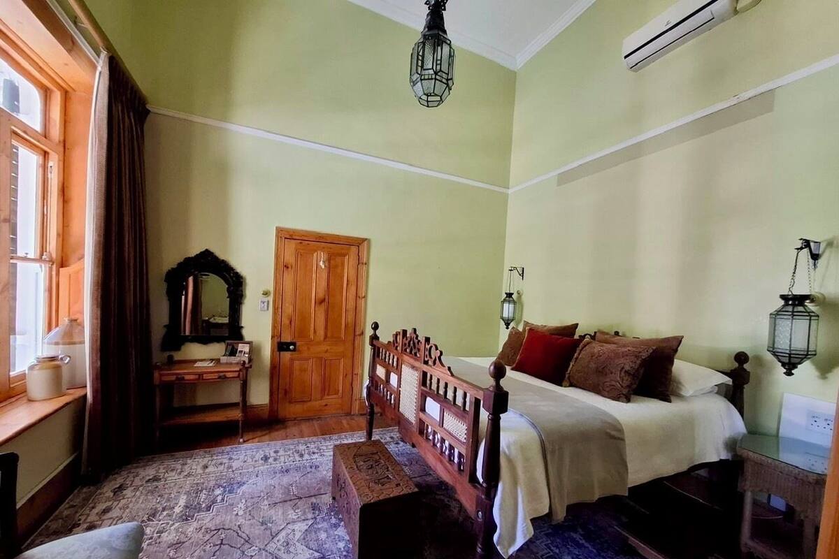 A traditional bedroom with a wooden bed, a nightstand, a bench, a mirror, and a window with curtains.