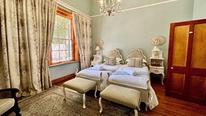 A bedroom with two beds, a chandelier, a wooden floor, and a large window with curtains. - Sundays Karoo Guesthouse (Graaff-Reinet)