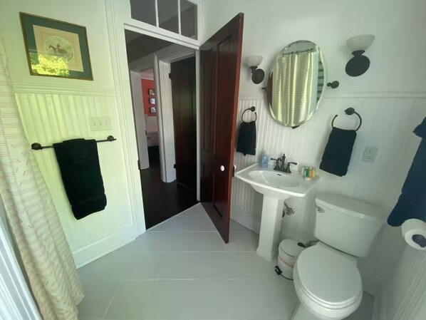 A bathroom with a toilet, sink, and mirror. There is a towel rack with a towel hanging on it. The bathroom has a door leading to another room. - Charming 3-bedroom house in Midway with screened in porch and salt water pool! (Midway)
