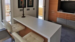 Eine moderne Küche mit weißem Arbeitsplatz, zwei Barhocker, einem Einbauofen und einem Fernseher.