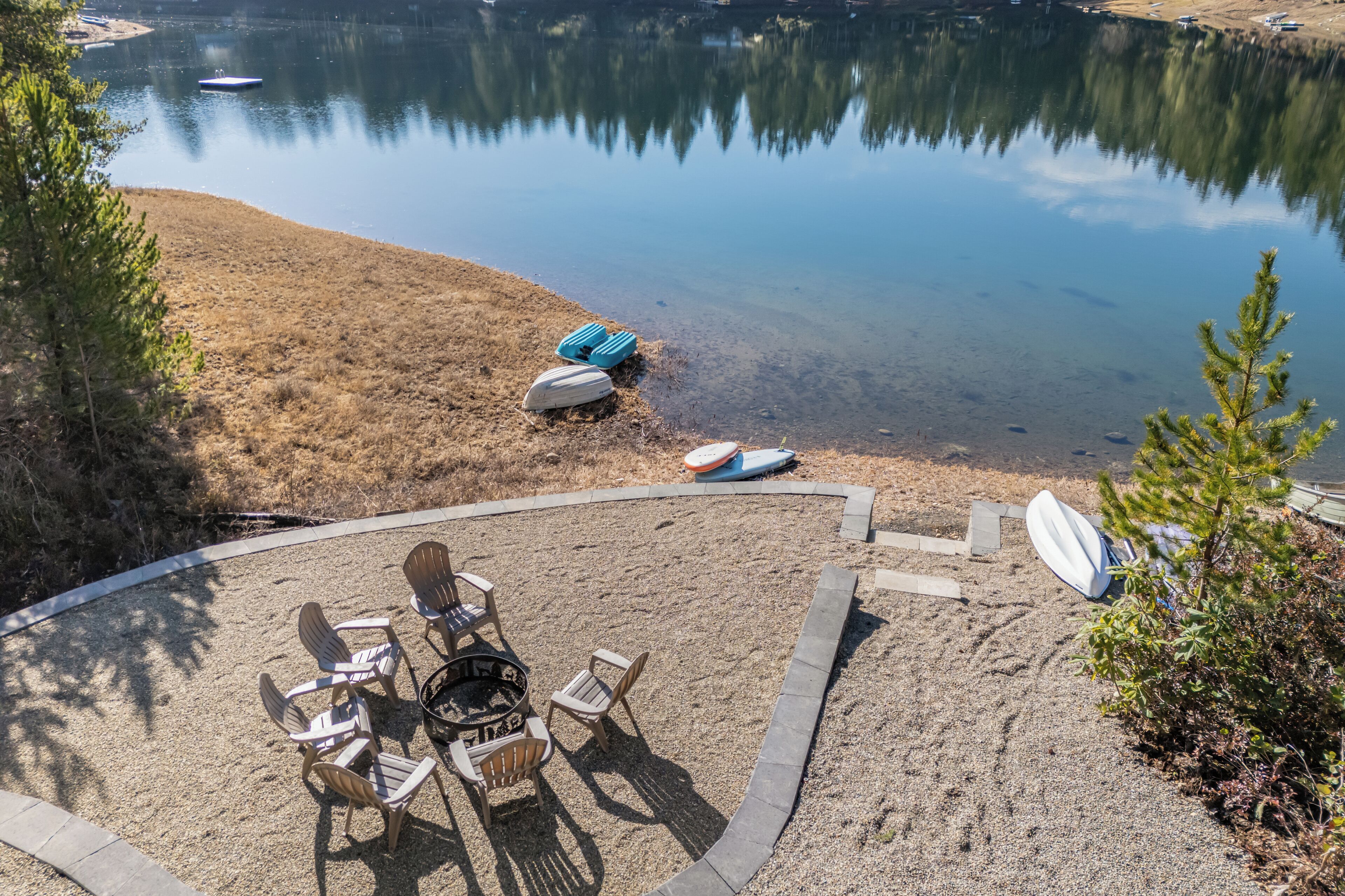 A circular outdoor seating area with chairs and a fire pit, overlooking a calm lake with boats.