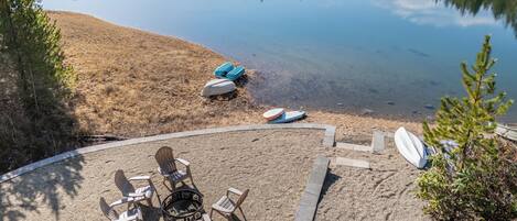 A circular outdoor seating area with chairs and a fire pit, overlooking a calm lake with boats.