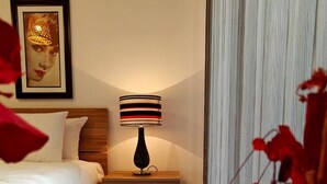 A modern bedroom with a wooden bed, a nightstand with a striped lamp, and a framed picture on the wall. - Charming 1-Bedroom Apartment in Il-Gżira, Malta (Il-Gżira)
