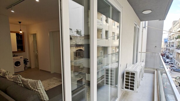 A modern apartment with a balcony, large sliding glass doors, and a view of the street. - Charming 1-Bedroom Apartment in Il-Gżira, Malta (Il-Gżira)