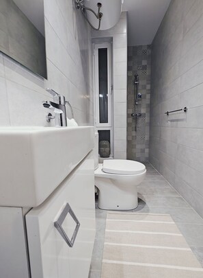 A modern bathroom with a white toilet, a glass-enclosed shower, and a large mirror above the sink.