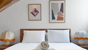 Ein Hotelzimmer mit einem ordentlich bezogenen Bett, zwei gerahmten Kunstwerken an der Wand und einem modernen Klimagerät.