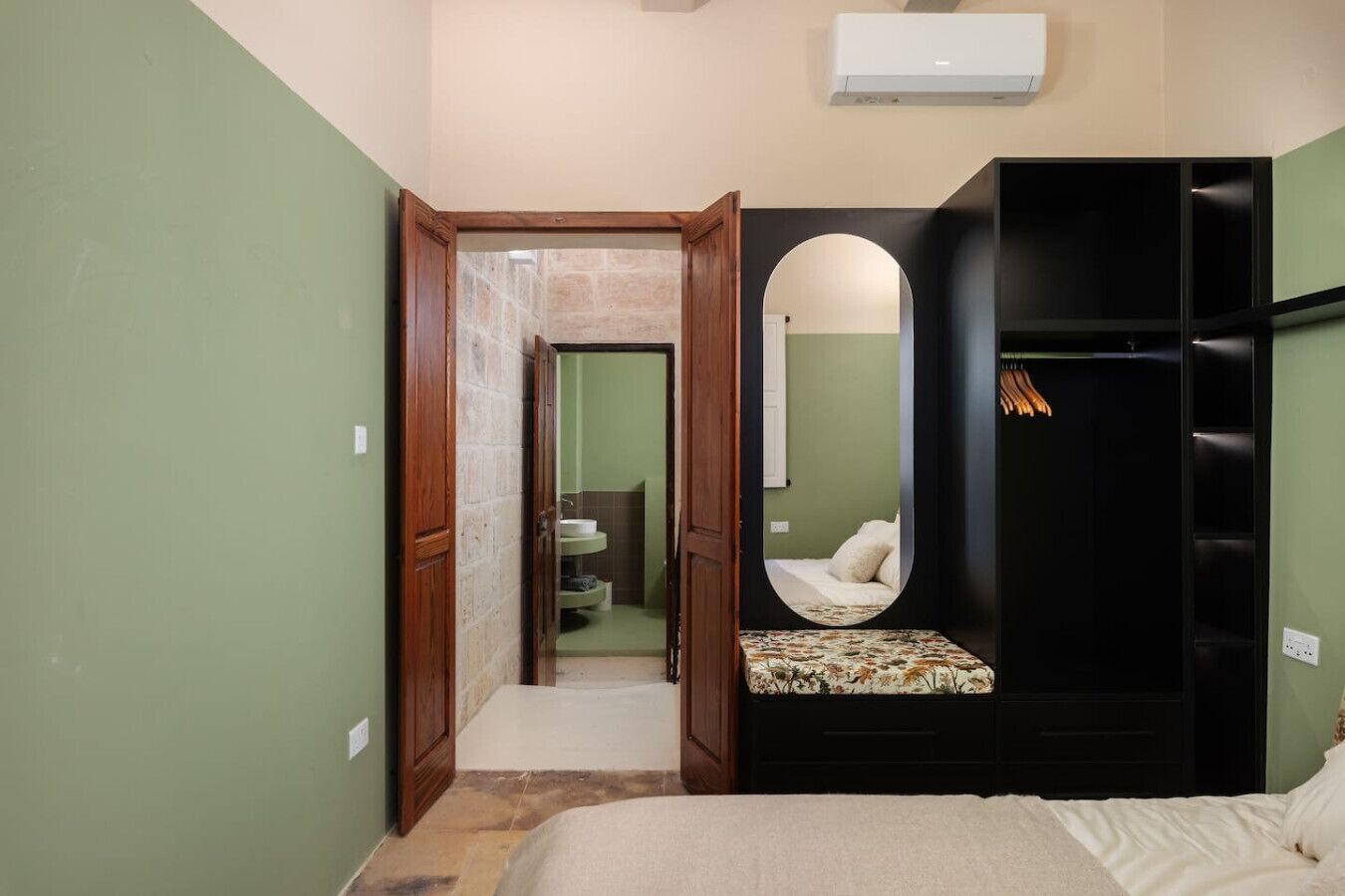 A bedroom with a bed, a mirror, a wardrobe, and a bathroom visible through an open door.