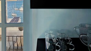 Une pièce avec vue sur la mer, visible par une fenêtre, une étagère noire avec des bocaux en verre et plusieurs verres à eau transparents posés sur une table.