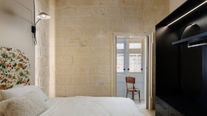 Une chambre avec un lit, une chaise, un téléviseur et un mur en pierre.