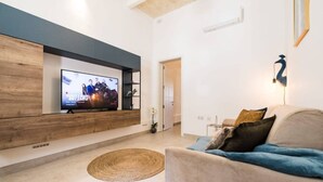 Una sala de estar moderna con un televisor de pantalla plana montado en una pared de paneles de madera, un sofá color beige con cojines, un tapete tejido y una pequeña planta en maceta.