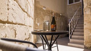 Una mesa con una botella de vino y dos copas, frente a una pared de piedra con una escalera de fondo.